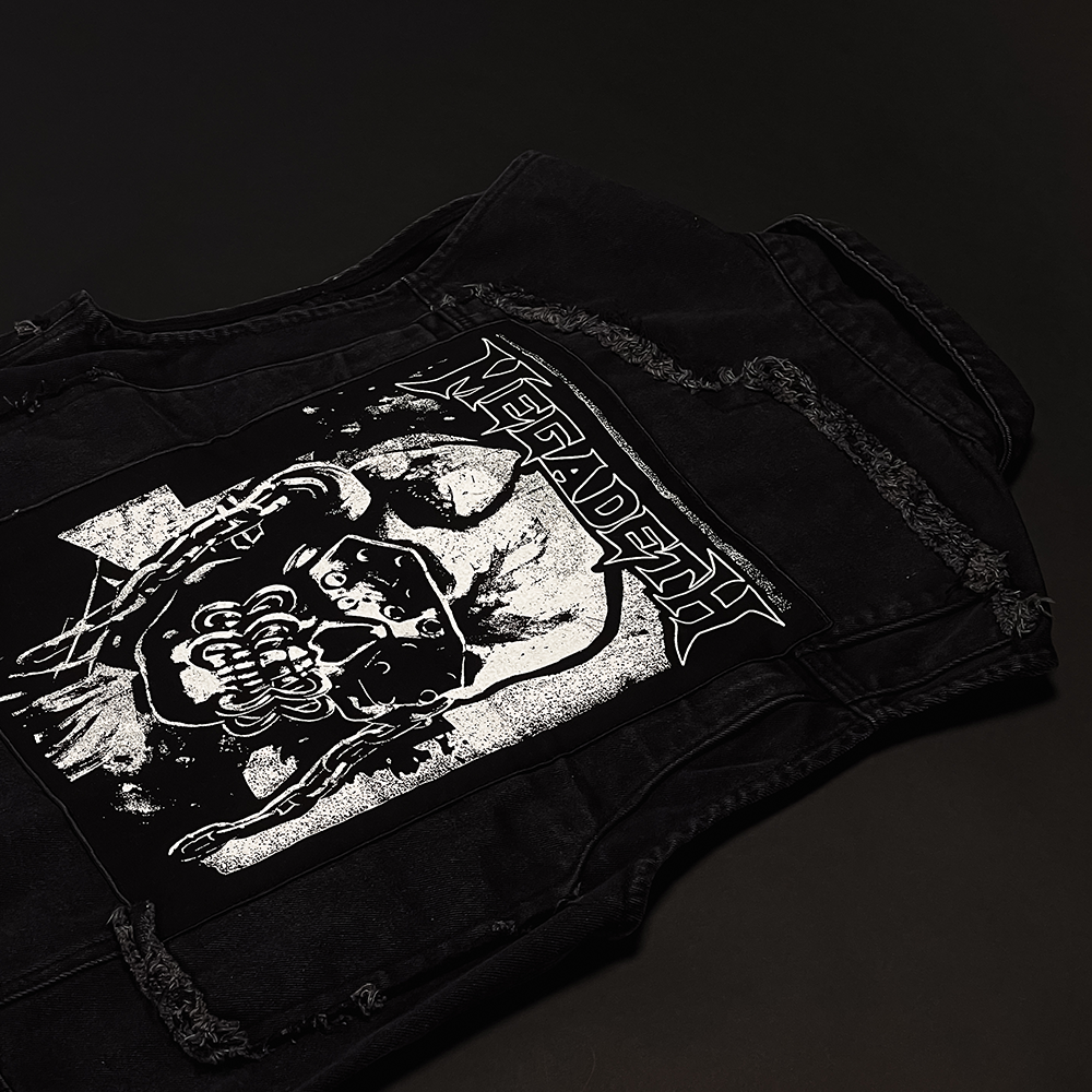 Official Megadeth Merchandise. Black button up denim vest with distressed details adorned with Megadeth pins and patches. The back features a large back patch with a silhouette of Vic.
